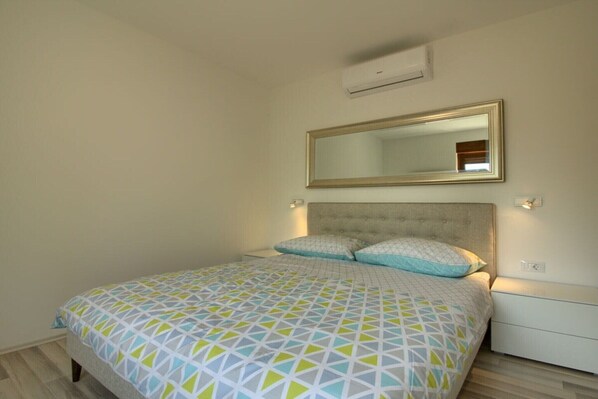 A bedroom with a bed, a headboard, a wall-mounted mirror, and a bedside table.