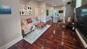 A spacious living room with a wooden floor, a sofa, a coffee table, and a television. - Home w/ Garden Oasis Walk to Lucas Oil Traeger Grill EV Charger (Indianapolis)