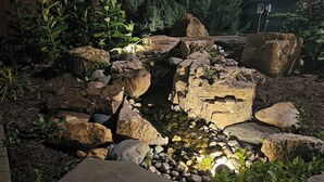A garden with a small water feature surrounded by rocks and plants. - Home w/ Garden Oasis Walk to Lucas Oil Traeger Grill EV Charger (Indianapolis)