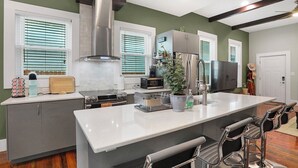 A modern kitchen with a central island, stainless steel appliances, and a bar area with stools. - Home w/ Garden Oasis Walk to Lucas Oil Traeger Grill EV Charger (Indianapolis)