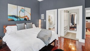 A modern bedroom with a large bed, a painting, and a view into another room. - Home w/ Garden Oasis Walk to Lucas Oil Traeger Grill EV Charger (Indianapolis)