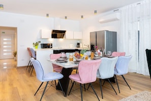 A modern dining area with a central table, chairs, and a kitchen in the background. - Luna & Pia Comfortable holiday residence (Pula)