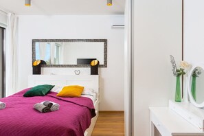 A bedroom with a bed, a bedside table, a mirror, and a window.