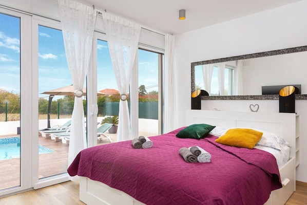 A bedroom with a large bed, a view of a pool, and a sliding glass door.