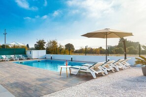 A swimming pool with lounge chairs and umbrellas, surrounded by a fence and trees.
