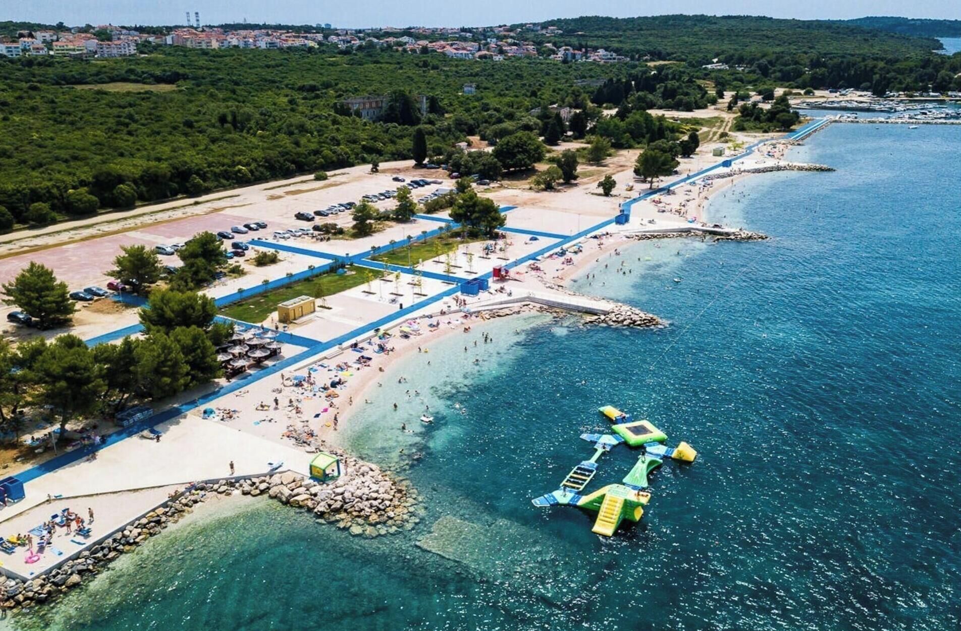 An aerial view of a coastal area with a beach, a parking lot, and a rocky shoreline.