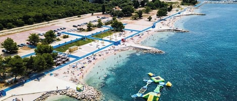 An aerial view of a coastal area with a beach, a parking lot, and a rocky shoreline.