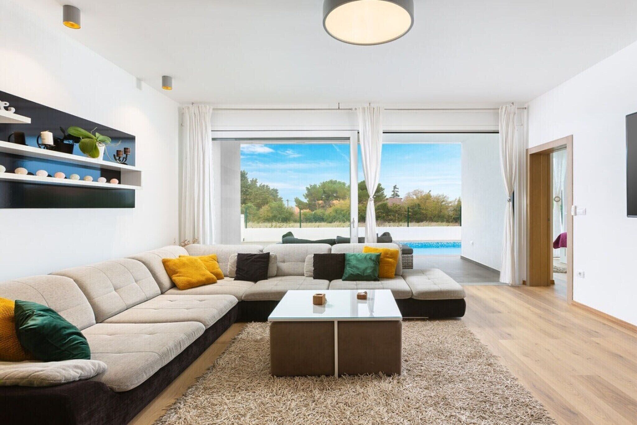 A modern living room with a sectional sofa, a glass coffee table, and a view of a swimming pool.