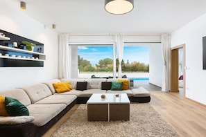 A modern living room with a sectional sofa, a glass coffee table, and a view of a swimming pool. - Luna & Pia Comfortable holiday residence (Pula)