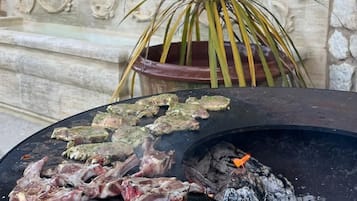 A grill with raw meat, a potted plant, and a stone wall.
