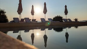 Una vista tranquilla a bordo piscina, con poltrone a sdraio e ombrelloni, che riflette il sole e il cielo sereno.