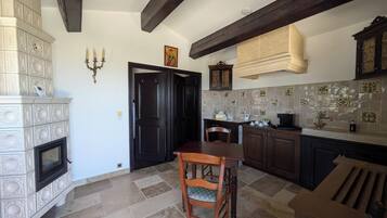 Una cocina con chimenea, vigas de madera oscura, salpicadero de azulejos y un comedor con mesa y sillas de madera.