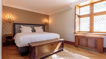 A bedroom with a large bed, a wooden chest, two wall sconces, and a window with a wooden frame.