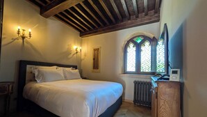 Una camera da letto con un letto, una testiera in legno, un comodino, una lampada a parete, un termosifone, una cassettiera in legno e una finestra con vetro colorato.