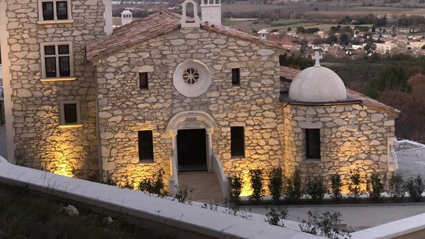 Un edificio in pietra con una cupola centrale e un campanile, immerso in un paesaggio collinare.
