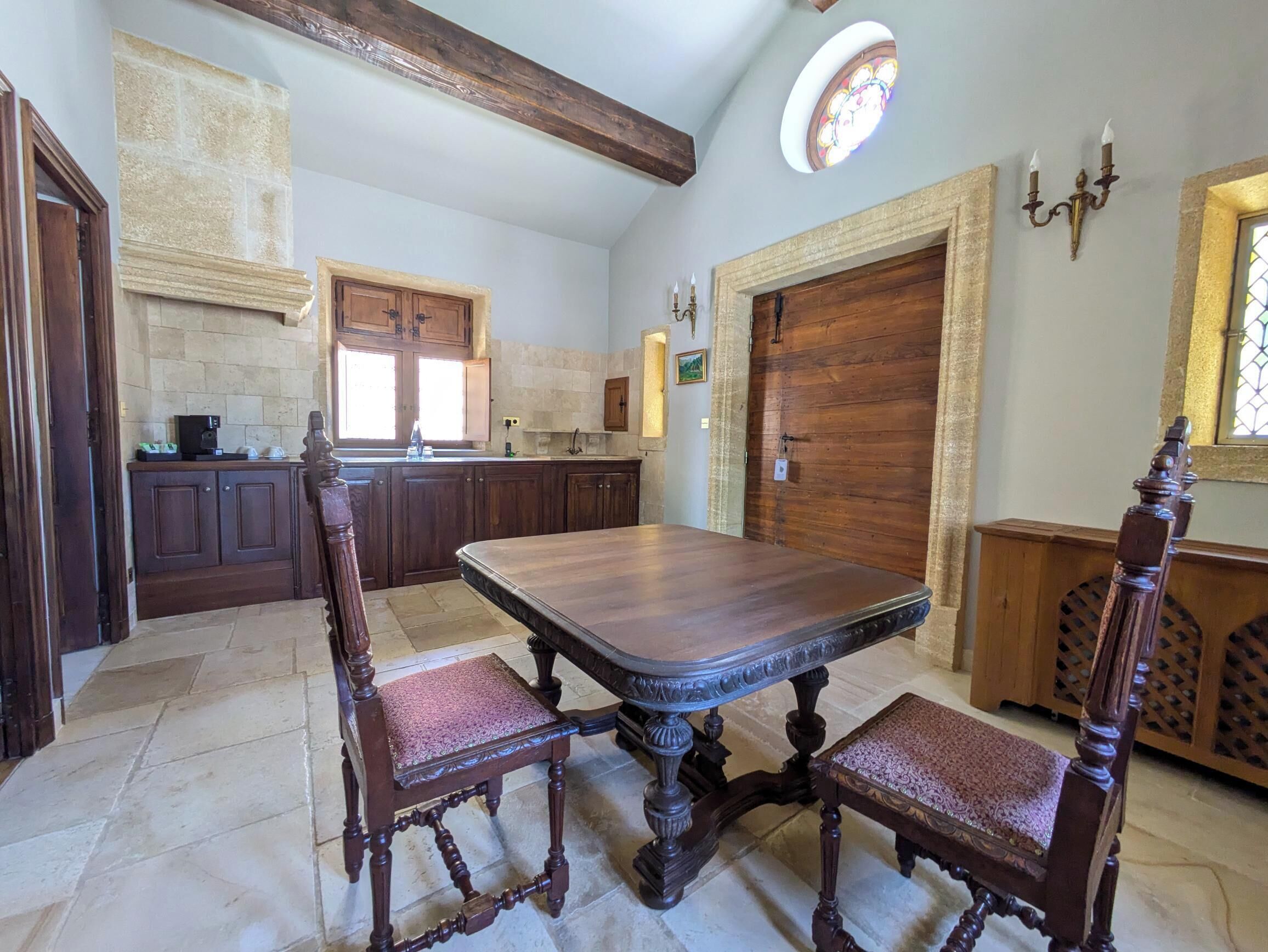 Uma cozinha ampla com uma grande mesa de madeira e cadeiras, paredes de pedra e uma porta de madeira.