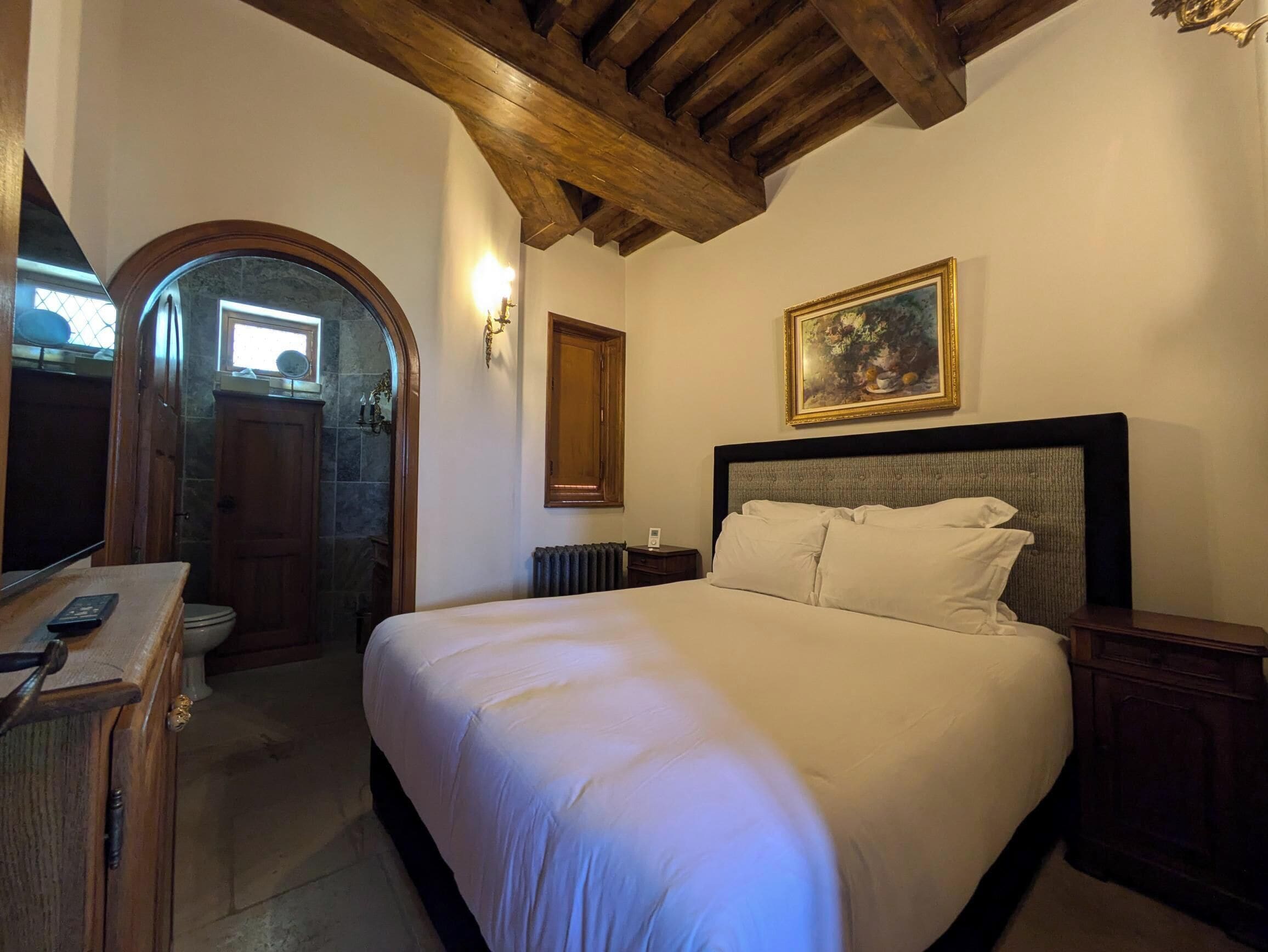 Une chambre avec un grand lit, une tête de lit en bois, un tableau et un plafond en bois.