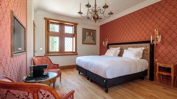 A bedroom with a large bed, a chandelier, a wooden floor, and patterned wallpaper.