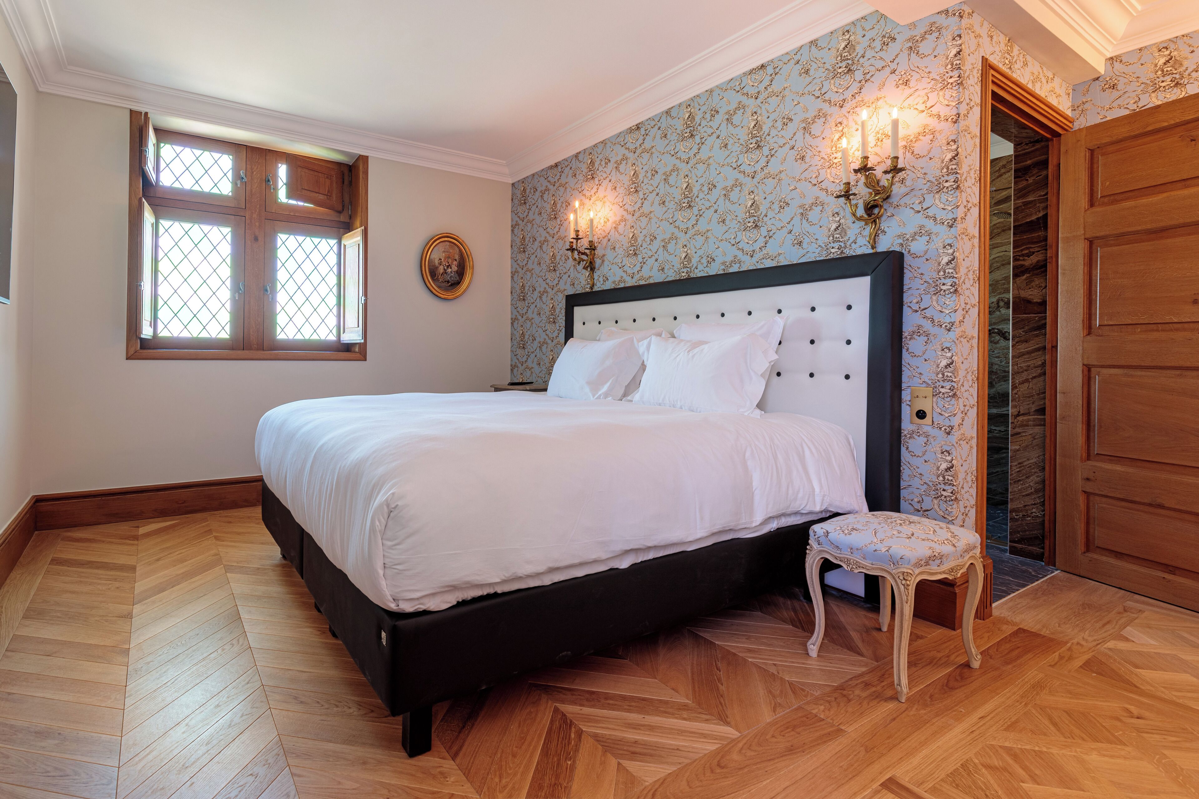 Un dormitorio con una cama grande, una silla pequeña, una ventana con vistas y una puerta.