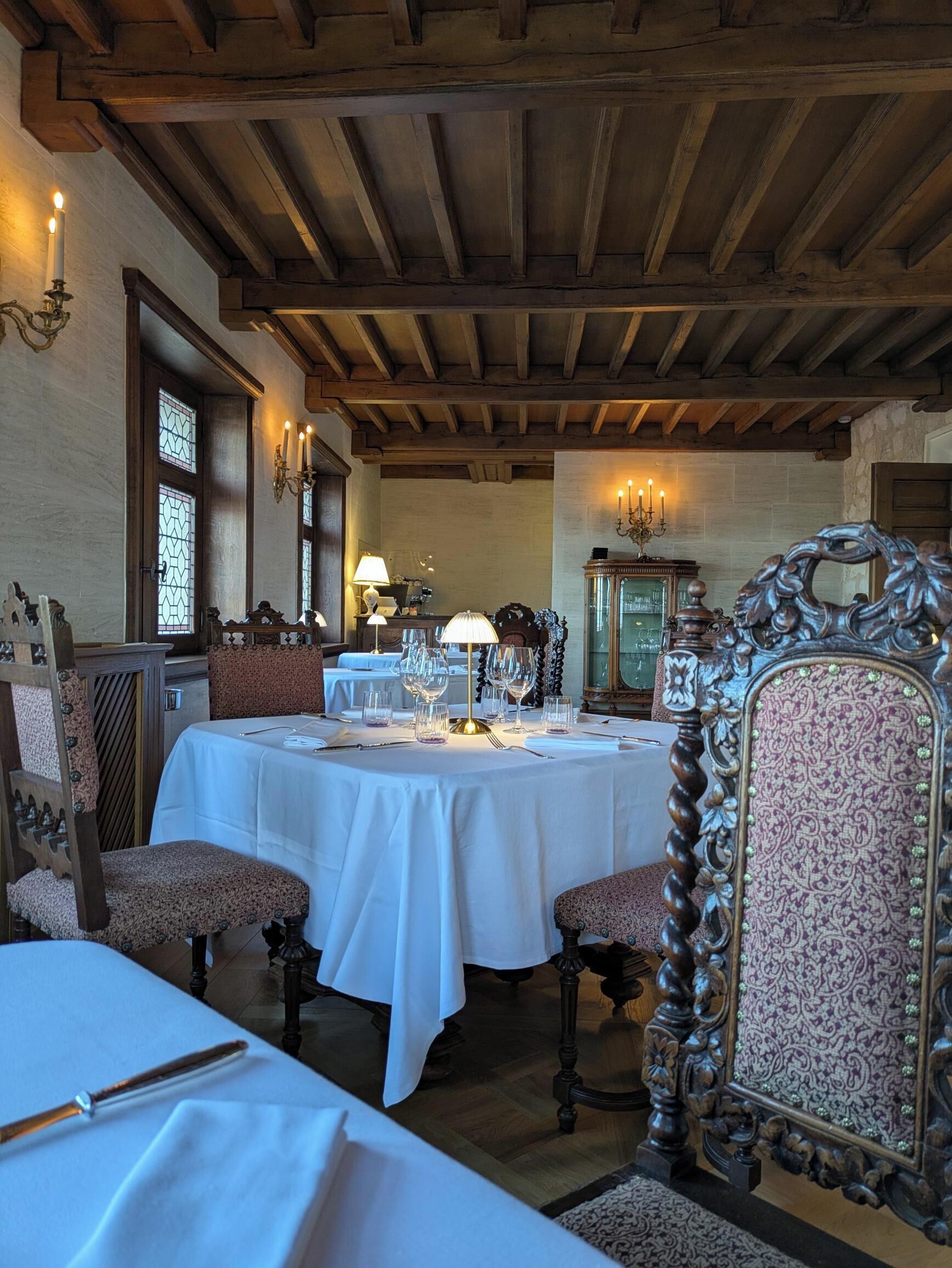 A dining area with a round table set for four, wooden beams on the ceiling, and a patterned chair.