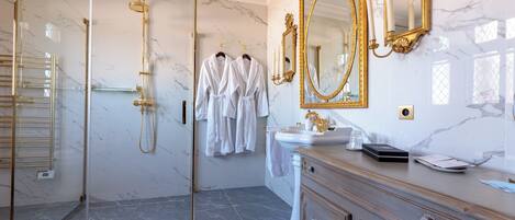 Un baño lujoso con ducha envuelta en vidrio, paredes de mármol y espejos con marcos de oro ornamentados.