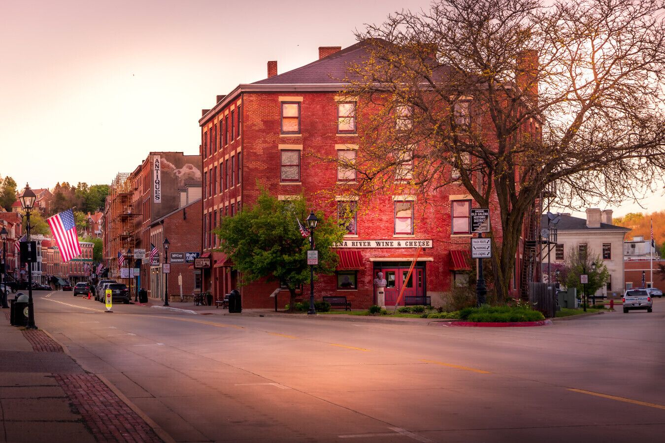 A historic building with a red brick facade, a prominent American flag, and a sign for 'River Wine & Cheese'.