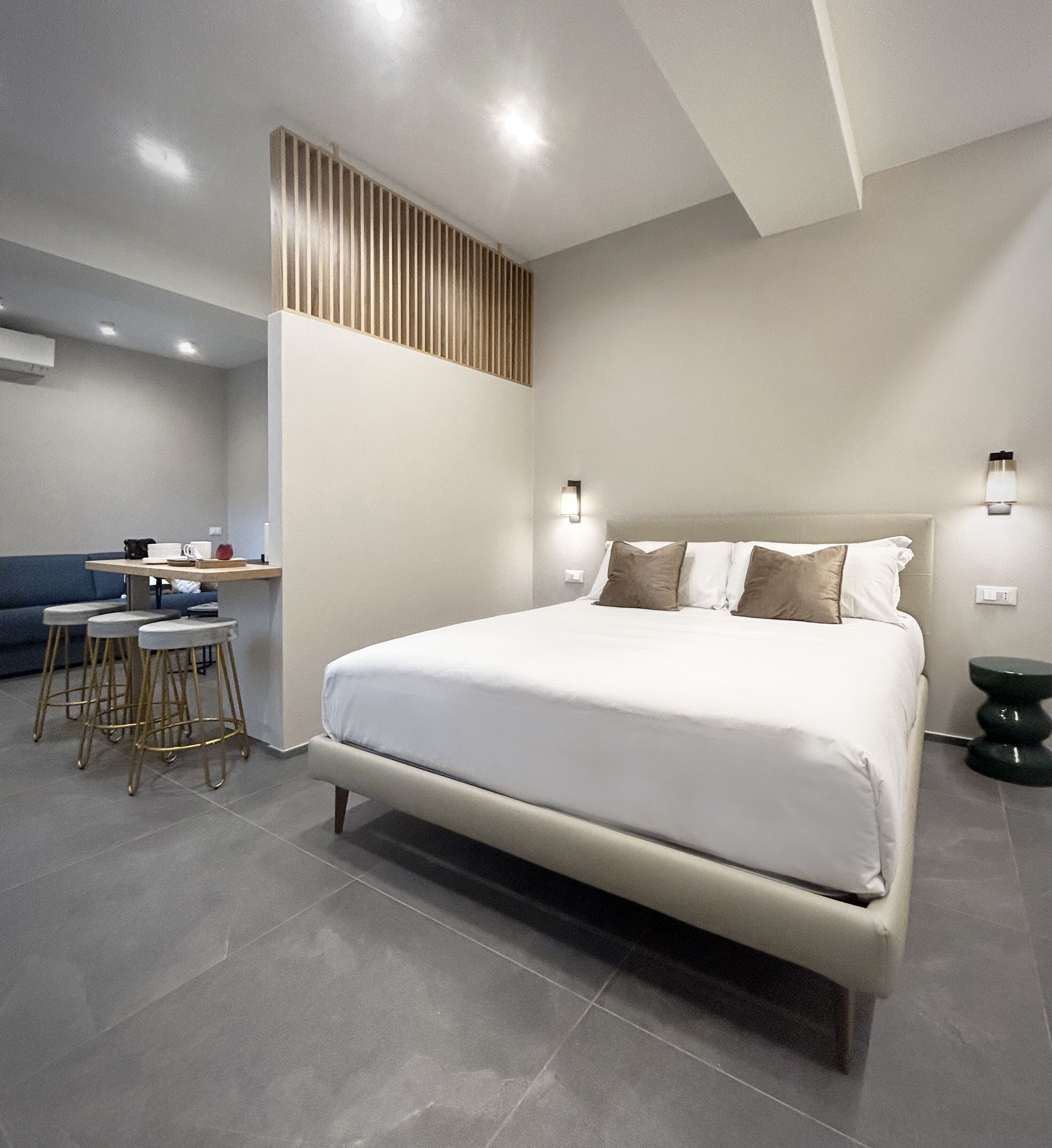 A modern bedroom with a large bed, a desk with a chair, and a stool.