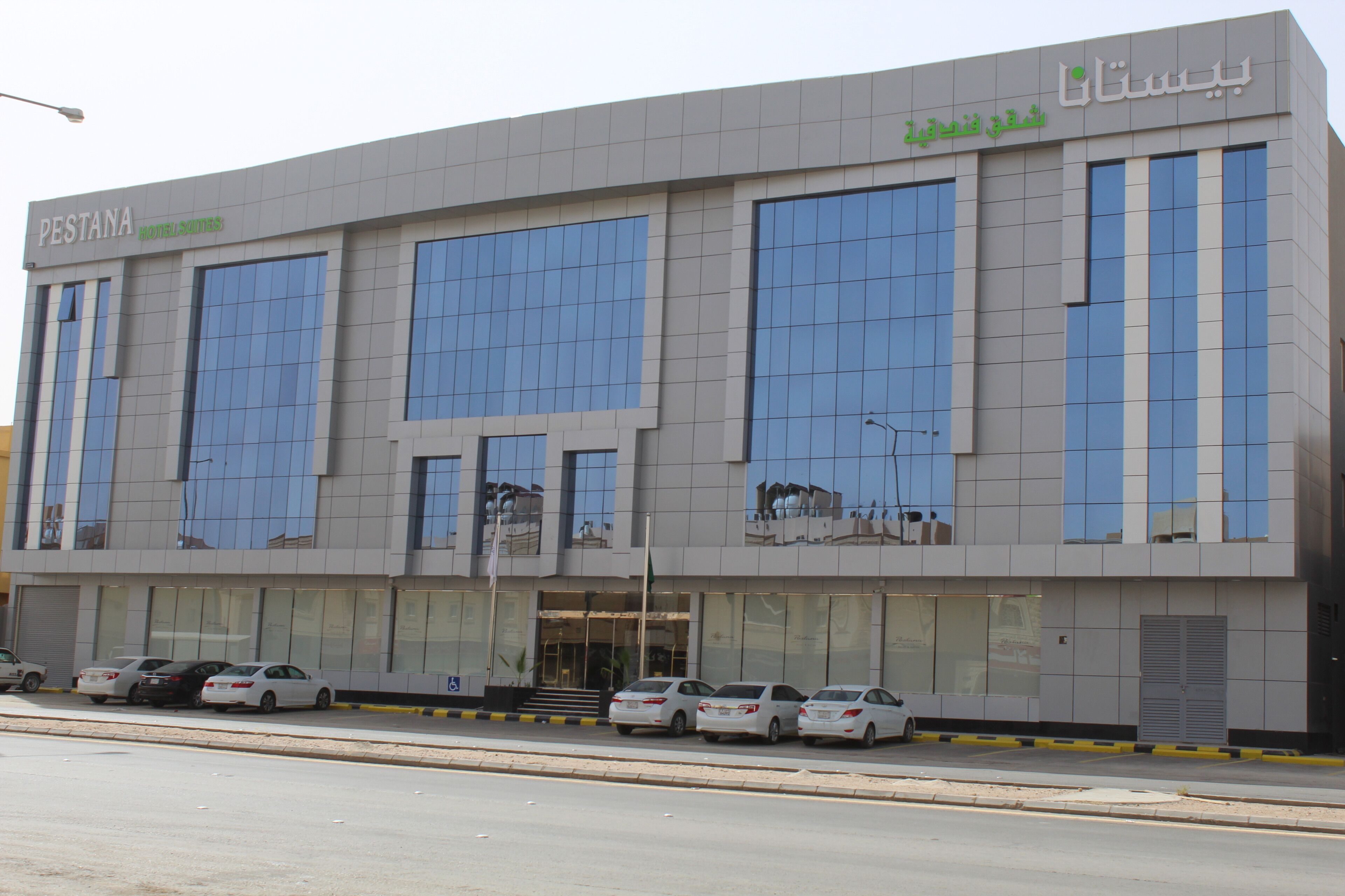 A modern hotel building with large windows and a parking lot.