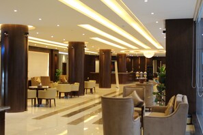 A modern hotel lobby with a polished marble floor, large wooden columns, and contemporary furniture. - Pestana Serviced Apartments. (Riyadh)