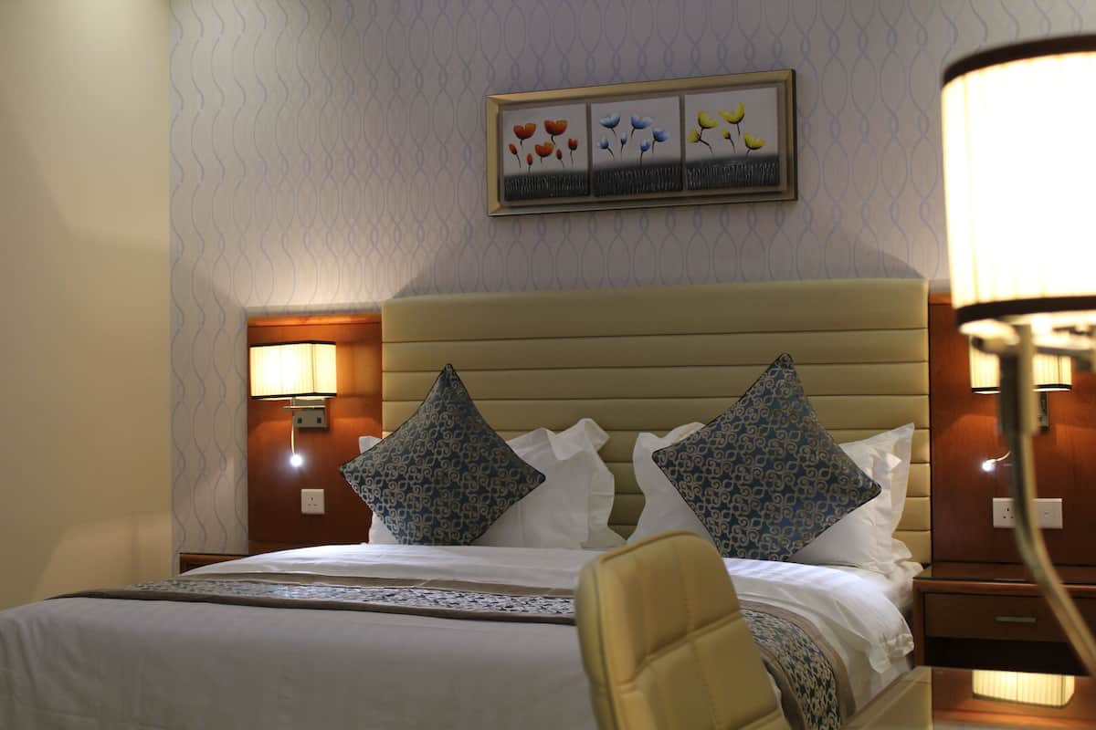 A hotel room with a bed, pillows, a nightstand, a lamp, and a wall-mounted artwork.