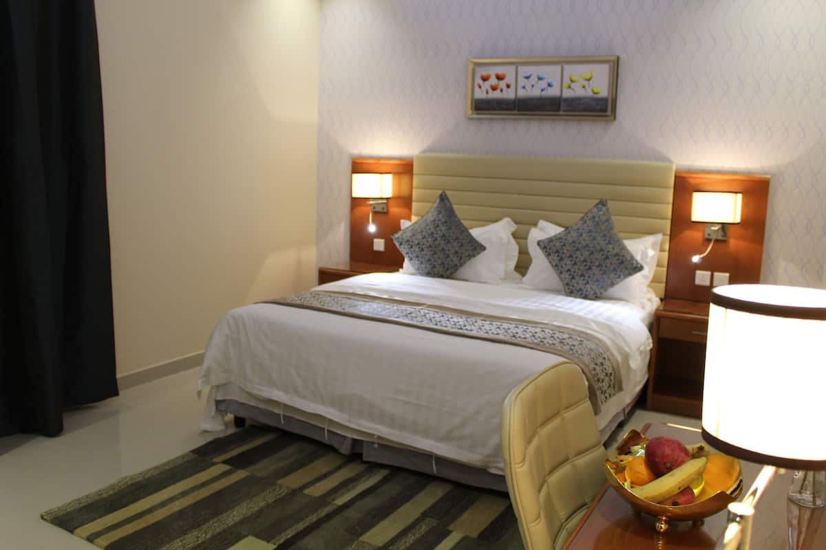 A hotel room with a bed, bedside lamps, a nightstand, a fruit bowl, and a wall-mounted picture.