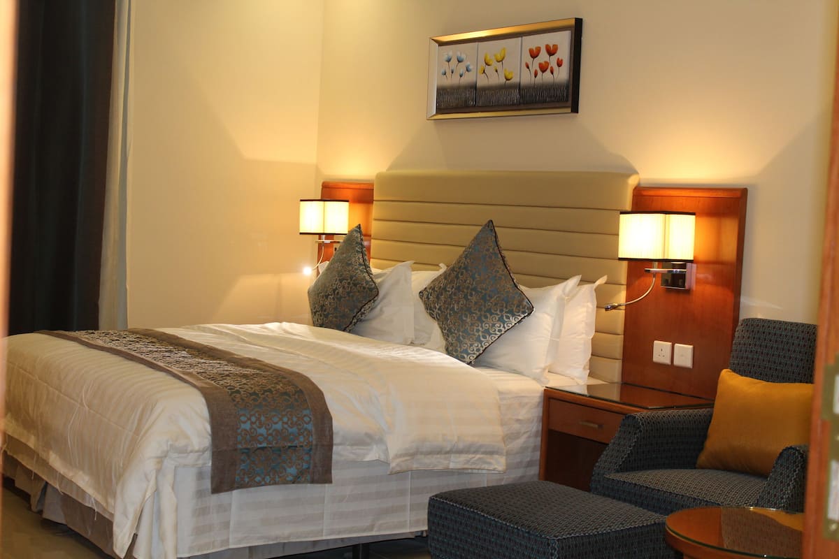 A hotel room with a large bed, two bedside lamps, a small table, and a chair.