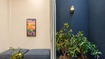 A room with a blue wall, a framed painting, a potted plant, and a seating area with cushions.