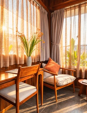 Ein Zimmer mit Holztisch und Stühlen, einer Topfpflanze und Blick durch große, mit Vorhängen drapierten Fenster.