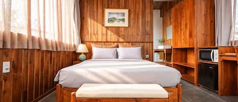 Una habitación con paneles de madera, con cama, mesita de noche, lámpara y microondas.