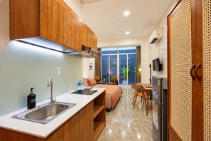 A modern kitchen with a built-in stove, a sink, and a refrigerator. There is a dining area with a table and chairs, and a sofa. - Nexus House Cay Diep - Near Independence Palace (Ho Chi Minh City)