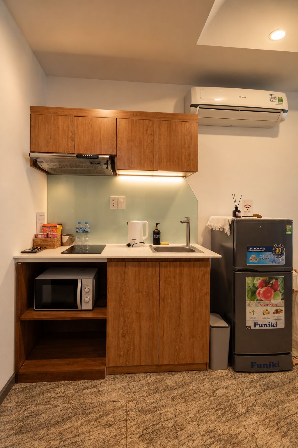 Una kitchenette compacta con armarios de madera, microondas, lavamanos y refrigerador.
