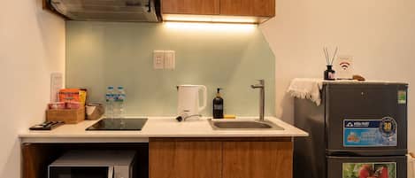 A compact kitchenette with wooden cabinets, a microwave, a sink, and a refrigerator.