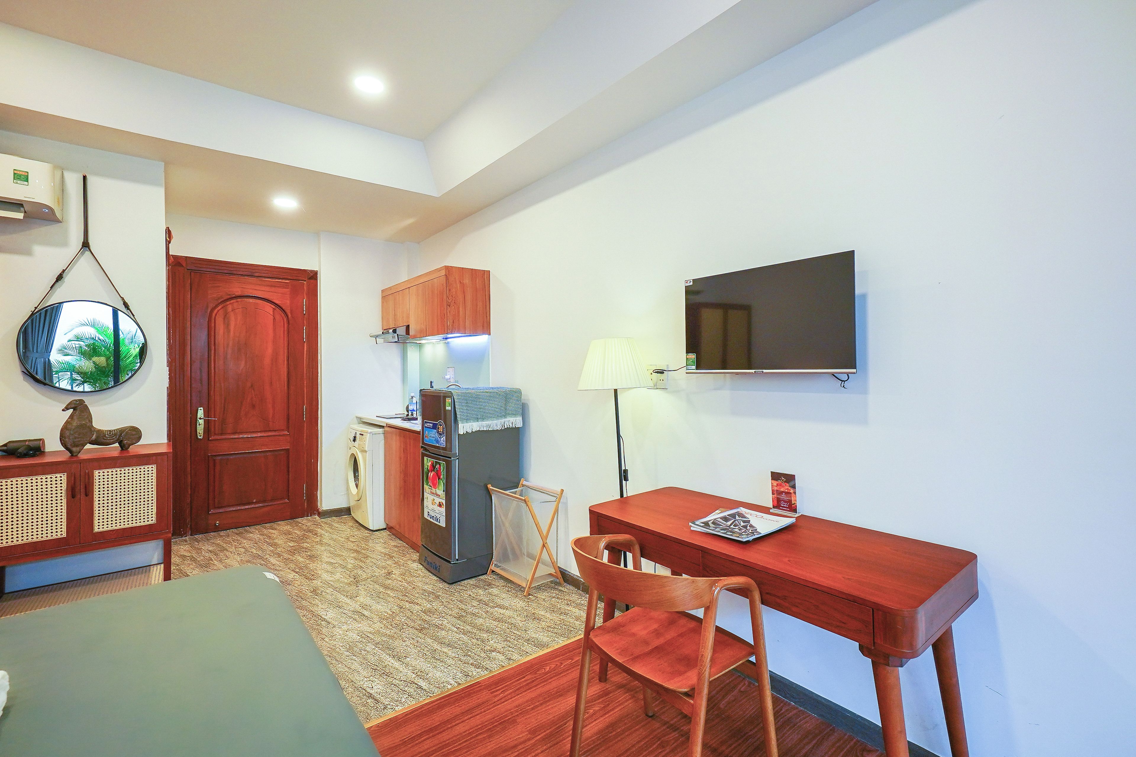Un espacio habitable compacto con una mesa de comedor, una silla, un refrigerador pequeño, una lavadora y un televisor montado en la pared.