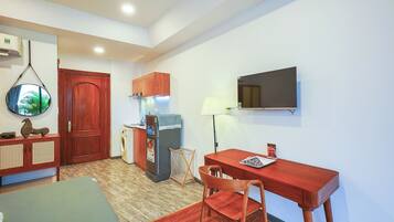 Un espacio habitable compacto con una mesa de comedor, una silla, un refrigerador pequeño, una lavadora y un televisor montado en la pared.