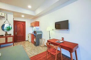 Un espacio habitable compacto con una mesa de comedor, una silla, un refrigerador pequeño, una lavadora y un televisor montado en la pared.