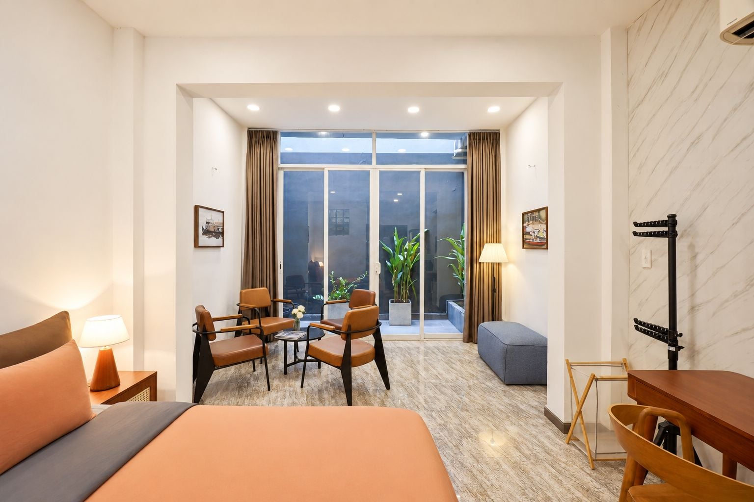 Habitación de hotel con cama, zona de estar, televisión y balcón con plantas.