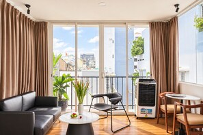 A modern living room with a sofa, a coffee table, a chair, a potted plant, and a view of the city through large windows. - Nexus House Cay Diep - Near Independence Palace (Ho Chi Minh City)