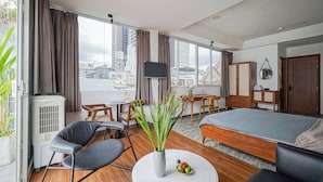 Una habitación de hotel moderna con una cama, una mesa redonda con un jarrón de flores, una silla, un escritorio con una silla, un televisor y vistas a la ciudad.