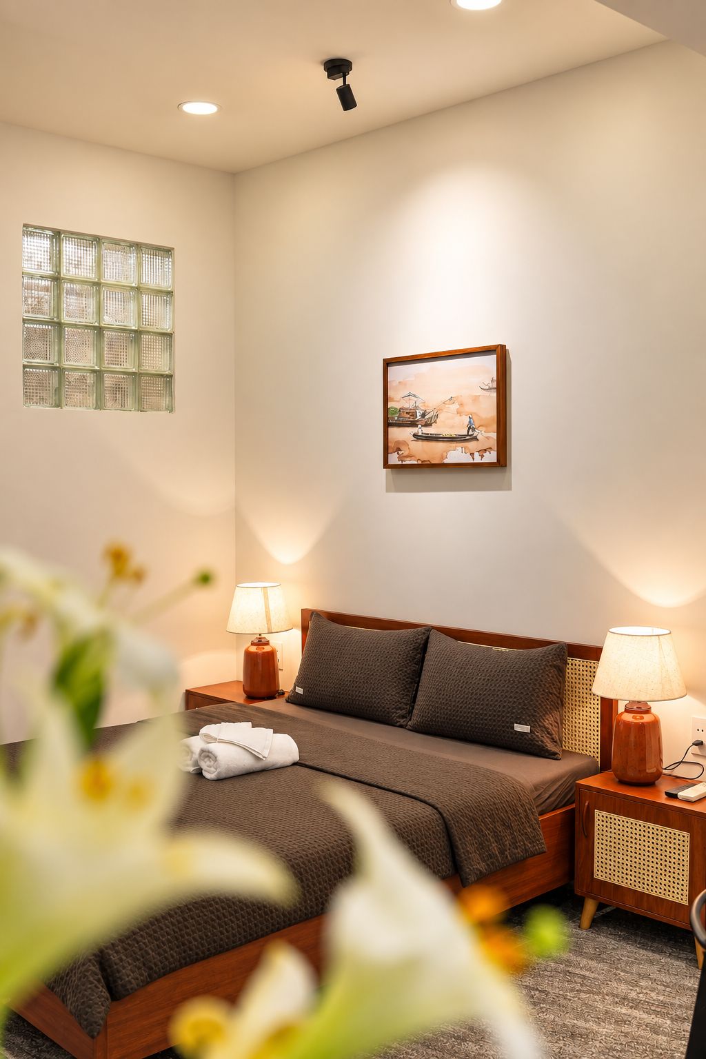 Une chambre d’hôtel avec un lit, deux lampes de chevet, une table de chevet, un tableau accroché au mur et une fenêtre avec des stores.