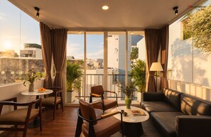 Una sala de estar moderna con un sofá, sillones, una mesa de centro y un balcón con plantas y vistas a la ciudad.