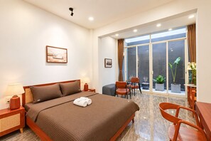 A hotel room with a large bed, two bedside tables with lamps, a seating area with chairs, a table, and a view through a large window. - Nexus House Cay Diep - Near Independence Palace (Ho Chi Minh City)