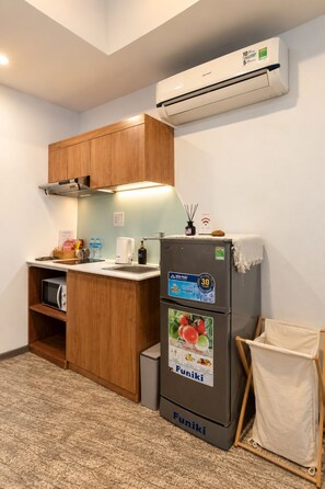 A compact kitchen with wooden cabinets, a built-in microwave, a refrigerator with a promotional sticker, and a wall-mounted air conditioner. - Nexus House Cay Diep - Near Independence Palace (Ho Chi Minh City)