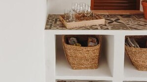 A hanging fruit basket with oranges and lemons, a wooden door, and wicker baskets on shelves. - Finca Viva la Vida (Álora)