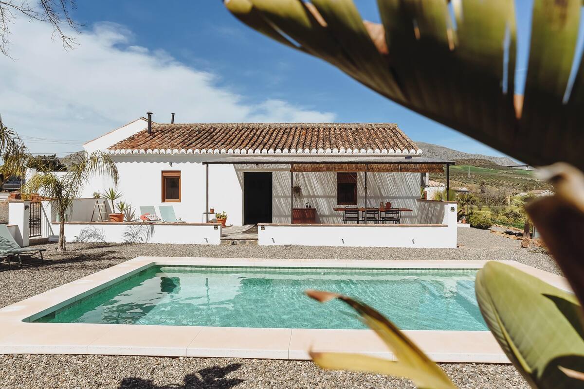A white house with a tiled roof, a swimming pool, and a patio area with outdoor furniture.